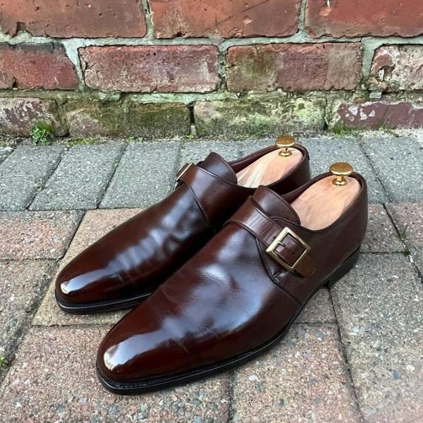 A pair of brown leather single-monk strap shoes against a brick wall, freshly conditioned and patina'd