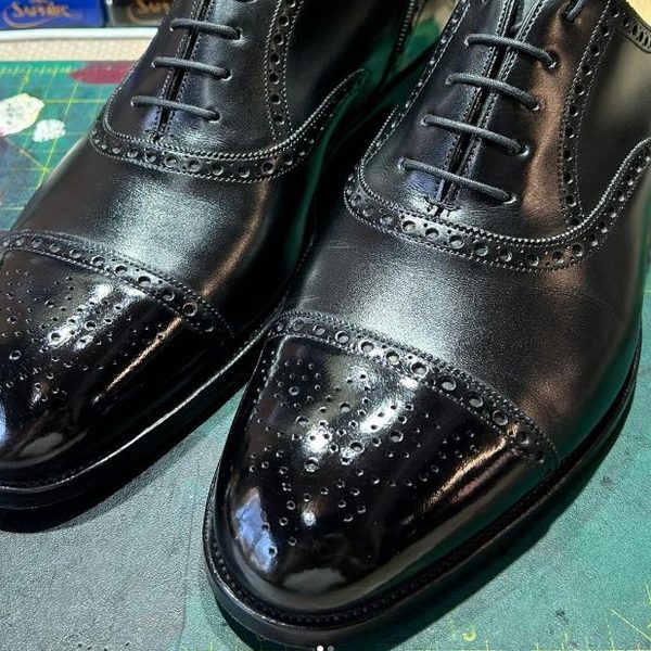 A pair of Crockett & Jones black brogue oxford shoes after a high-shine glaçage on the toecap