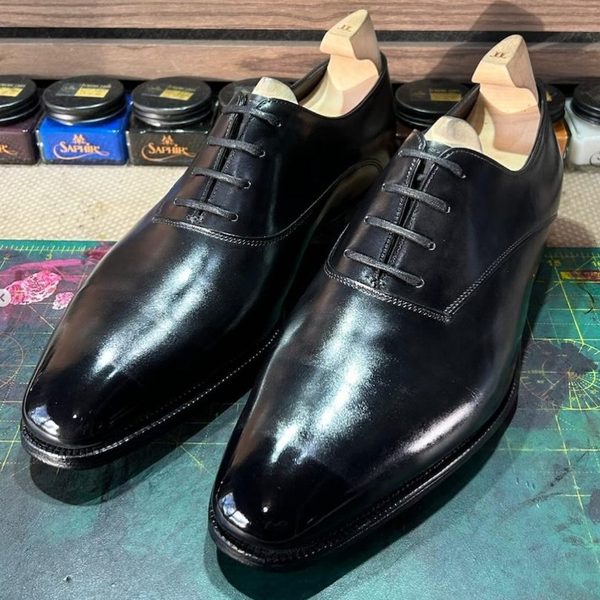 A pair of black wholecut oxford shoes after a glaçage mirror finish, Saphir Médaille d'Or polishes visible behind