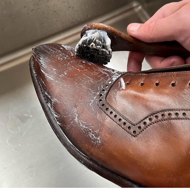 Cleansing a brown leather brogue with a horsehair brush and Saphir cleaner — step two of the Spitshine shoe care process