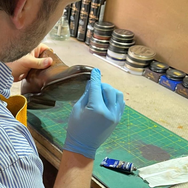 Heel edge being finished by hand against a wall of Saphir Médaille d'Or polish tins at the Spitshine workshop