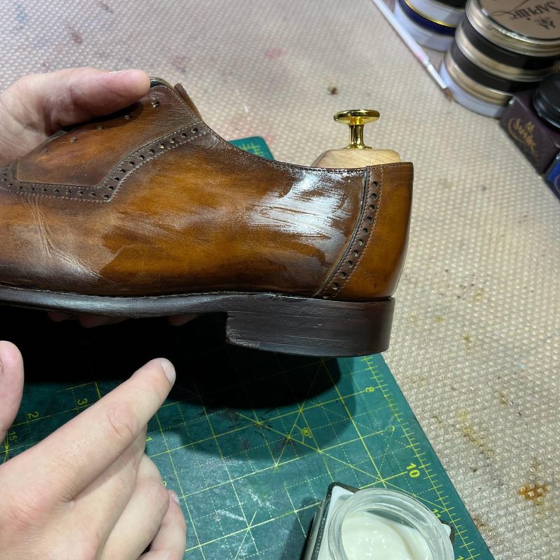 Leather conditioning cream applied to a patina'd oxford on a wooden shoe tree, Saphir cream pot beside it