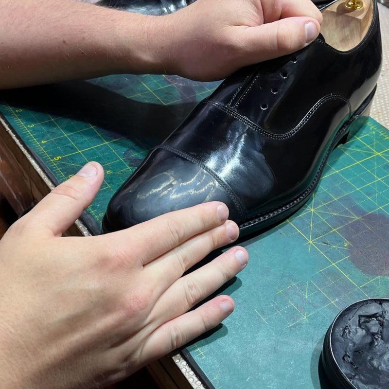 Glaçage mirror finish being built up by hand on the toecap of a black oxford — the seventh and final step of the Spitshine ritual